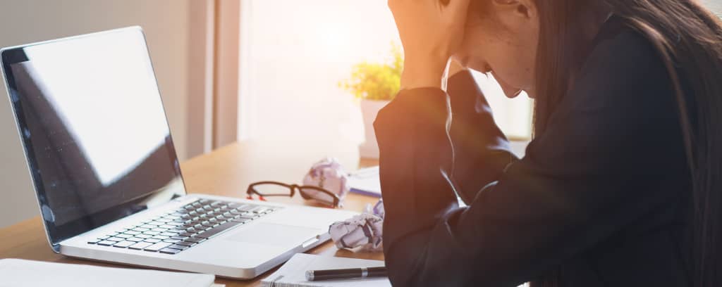 Photo of small business owner exhibiting despair with her head bowed and in her hands.