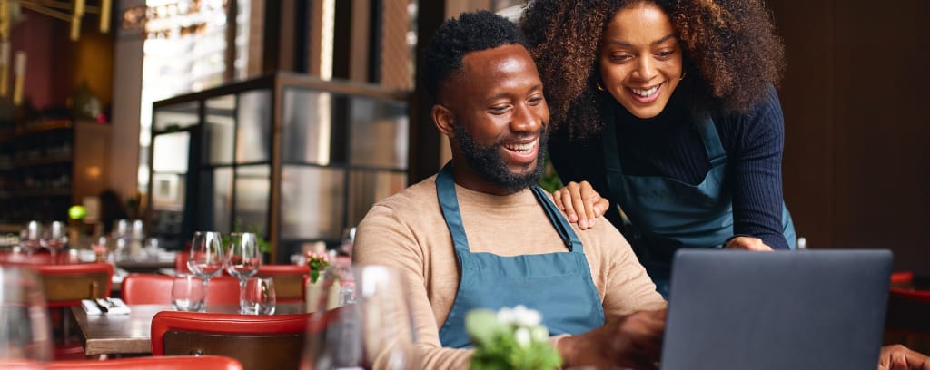 Black small business owners looking at laptop computer screen and smiling.