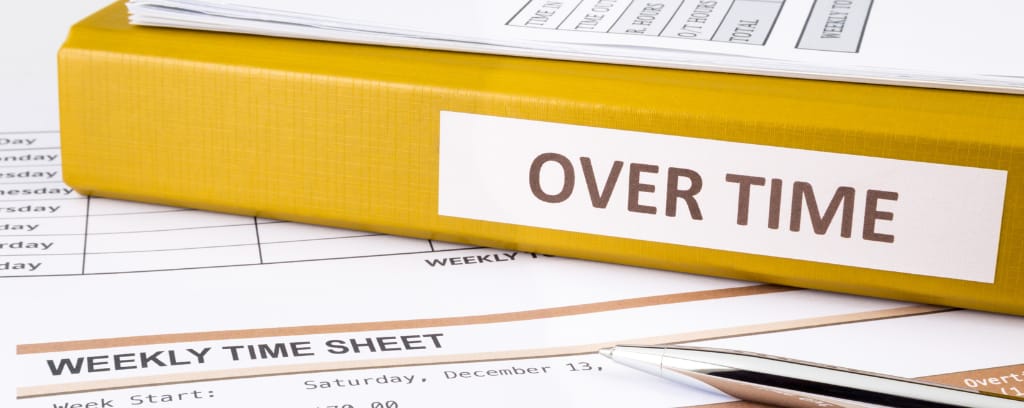 Photo of yellow binder marked "overtime" and sitting atop an employee timesheet