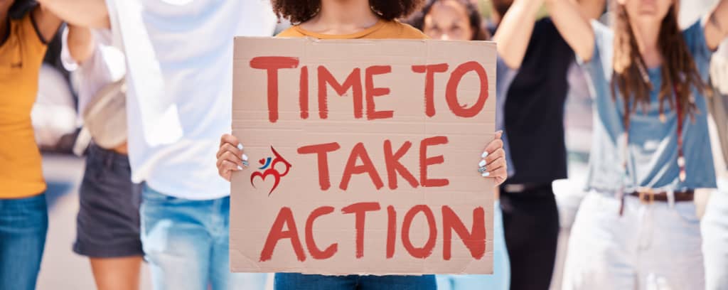 Photo of protesters. In the center is a sign reading "Time to take action."