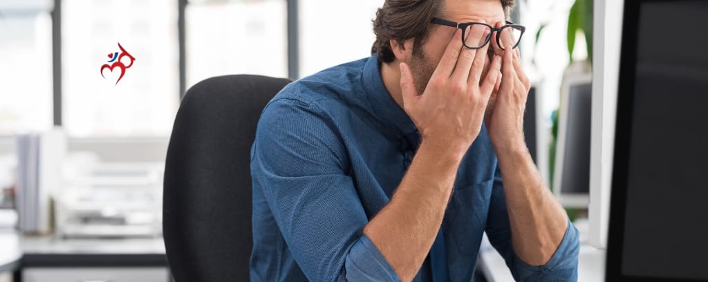 Photo of worker at desk with hands covering face and glasses shoved up on forehead