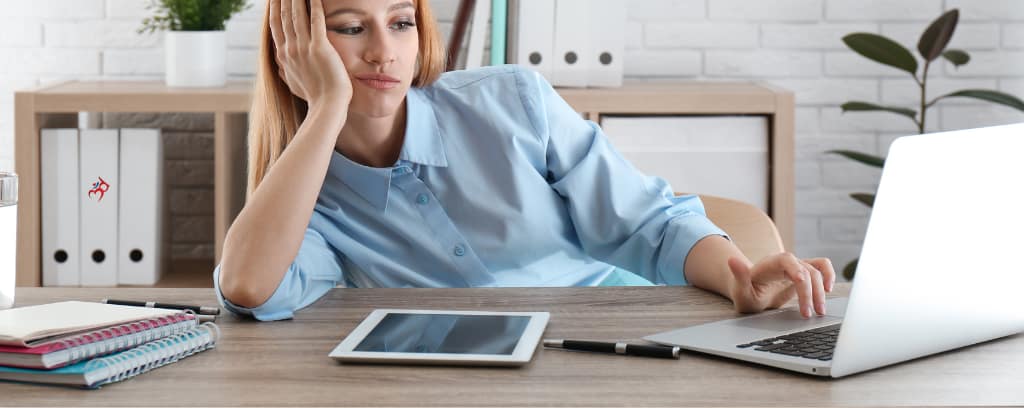 Photo of worker with head propped up on desk with one hand and boredom expression