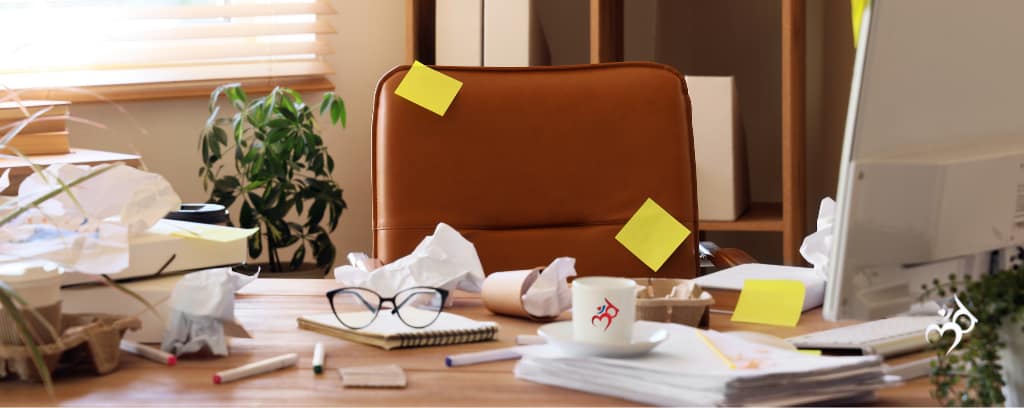 Photo of messy office desk with papers, sticky notes, coffee cup, eyeglasses, etc.