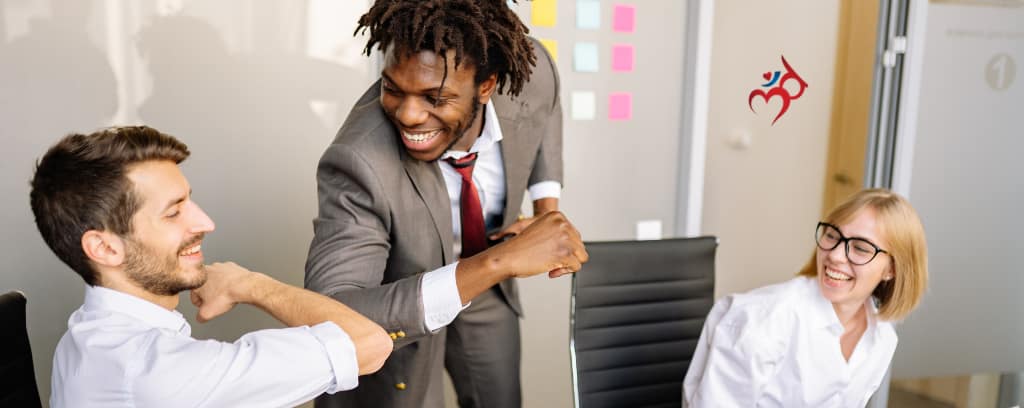 Photo of smiling boss bumping elbows with smiling employee while co-worker smiles