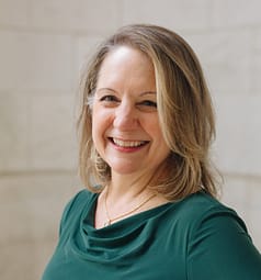 Nance Schick smiling and wearing green dress outside New York Public Library in Midtown Manhattan