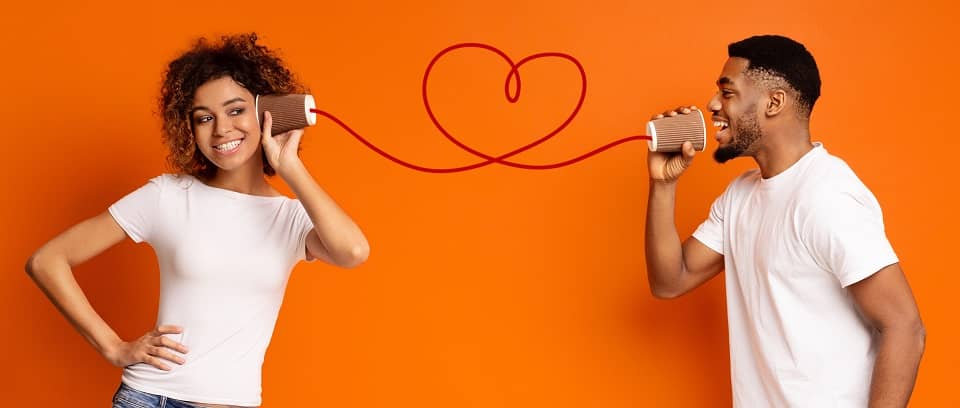 Photo of two people working well together by playing the telephone game in which they speak to each other through cans connected by a string that curls into a heart.