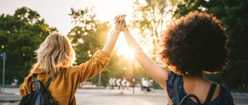 Coworkers holding hands and raising them between them as the sun sets in the background.