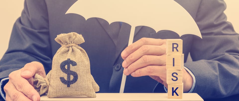 Photo of business owner holding umbrella over bag of money and blocks spelling risk