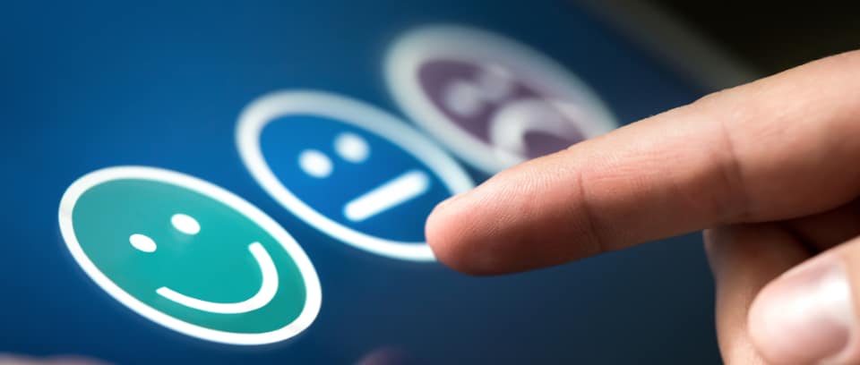 Photo of finger preparing to give feedback by choosing a happy, neutral, or sad face icon