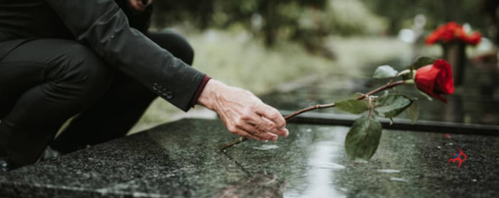 Photo of funeral director placing a red rose on a casket