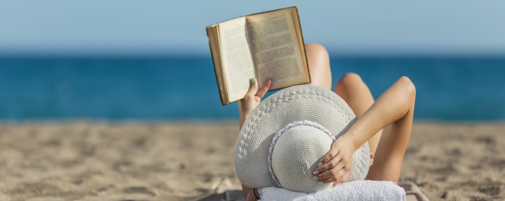 Photo of person lying on a beach and reading a book