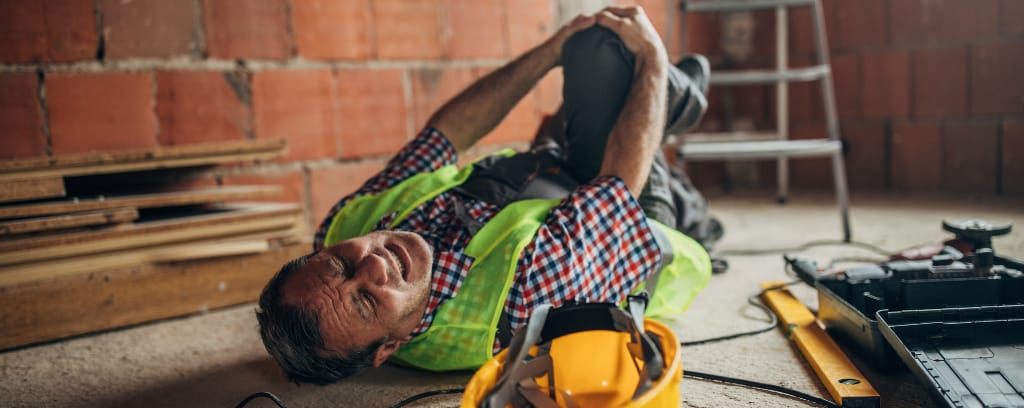 Photo of construction worker lying on his back and holding his right knee