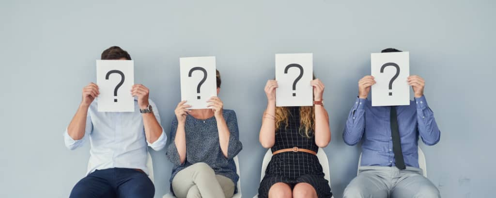 Photo of four people sitting with their faces obscured by signs with question marks