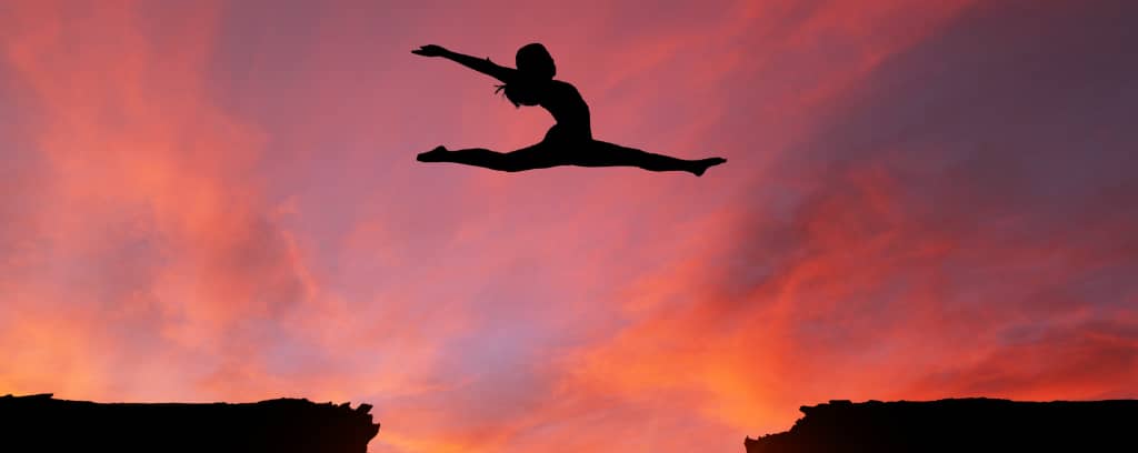 Photo of person leaping from ledge to ledge as the sun sets