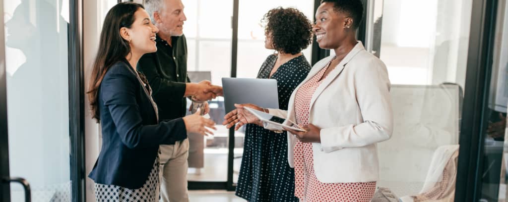 Diverse group of four employees smiling and greeting each other.