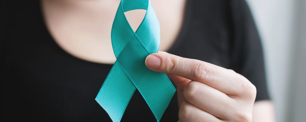 Photo of person in a black T-shirt holding teal sexual assault awareness ribbon toward the camera.