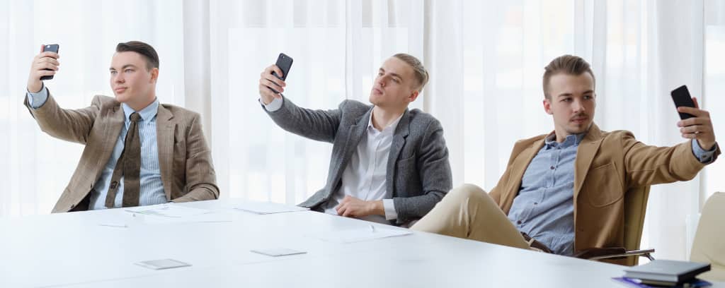 Photo of three people taking selfies around a conference table