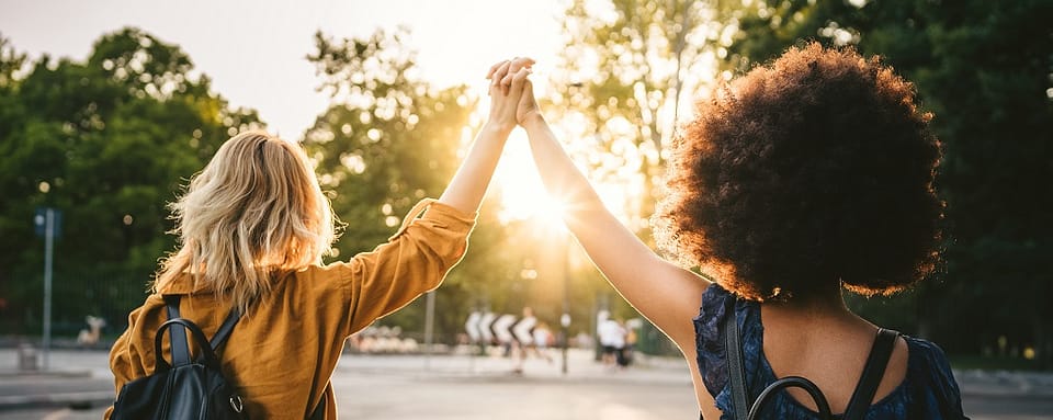 Coworkers holding hands and raising them between them as the sun sets in the background.